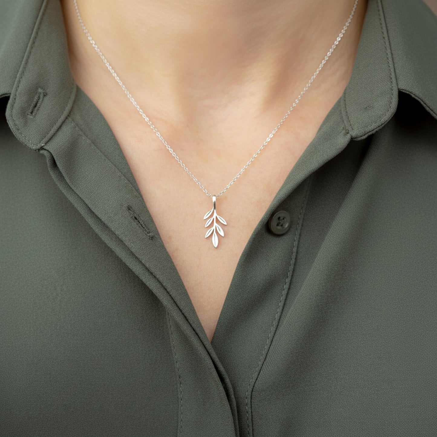 Silver necklace olive branch pendant worn by a person in a green shirt.