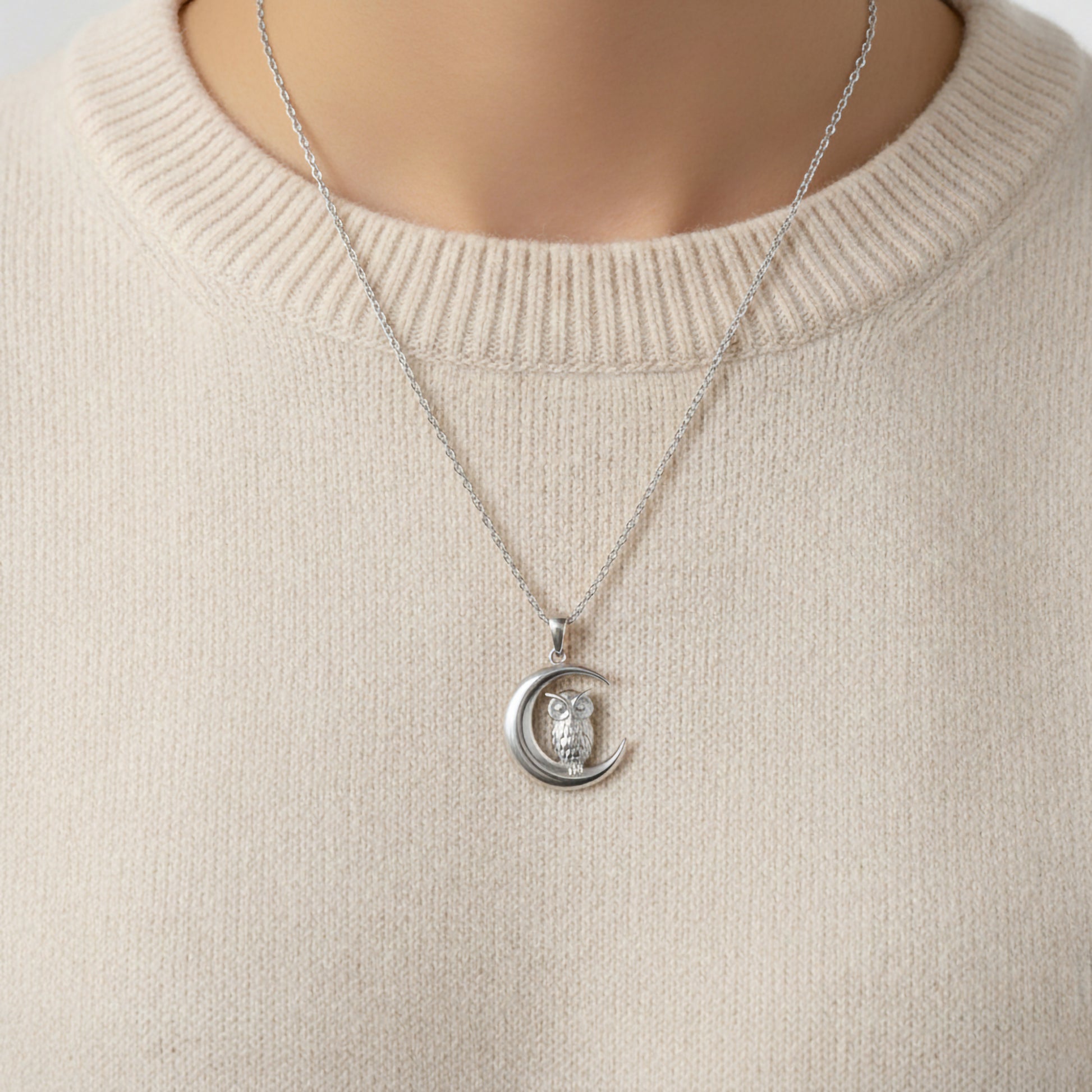 Silver necklace with a crescent moon and owl pendant on a beige sweater.