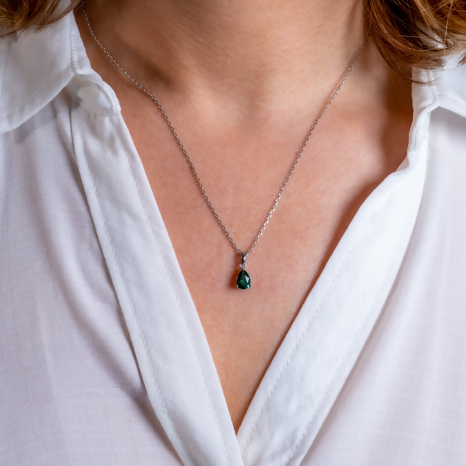 Close-up of a necklace with a green pendant worn by a person in a white shirt.