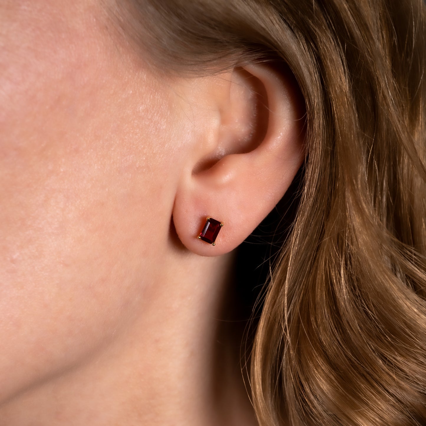 Close-up of an ear with lab ruby earring against a neutral background