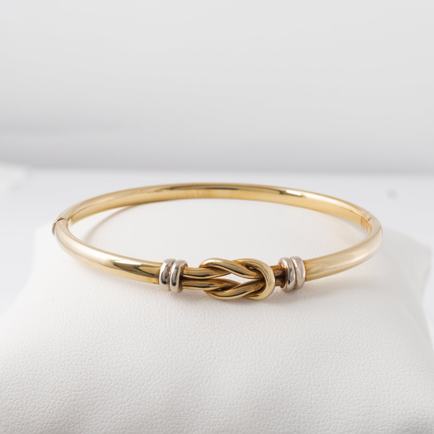 Front view of a 9ct gold lovers knot bangle with white gold accents, displayed on a cushioned surface