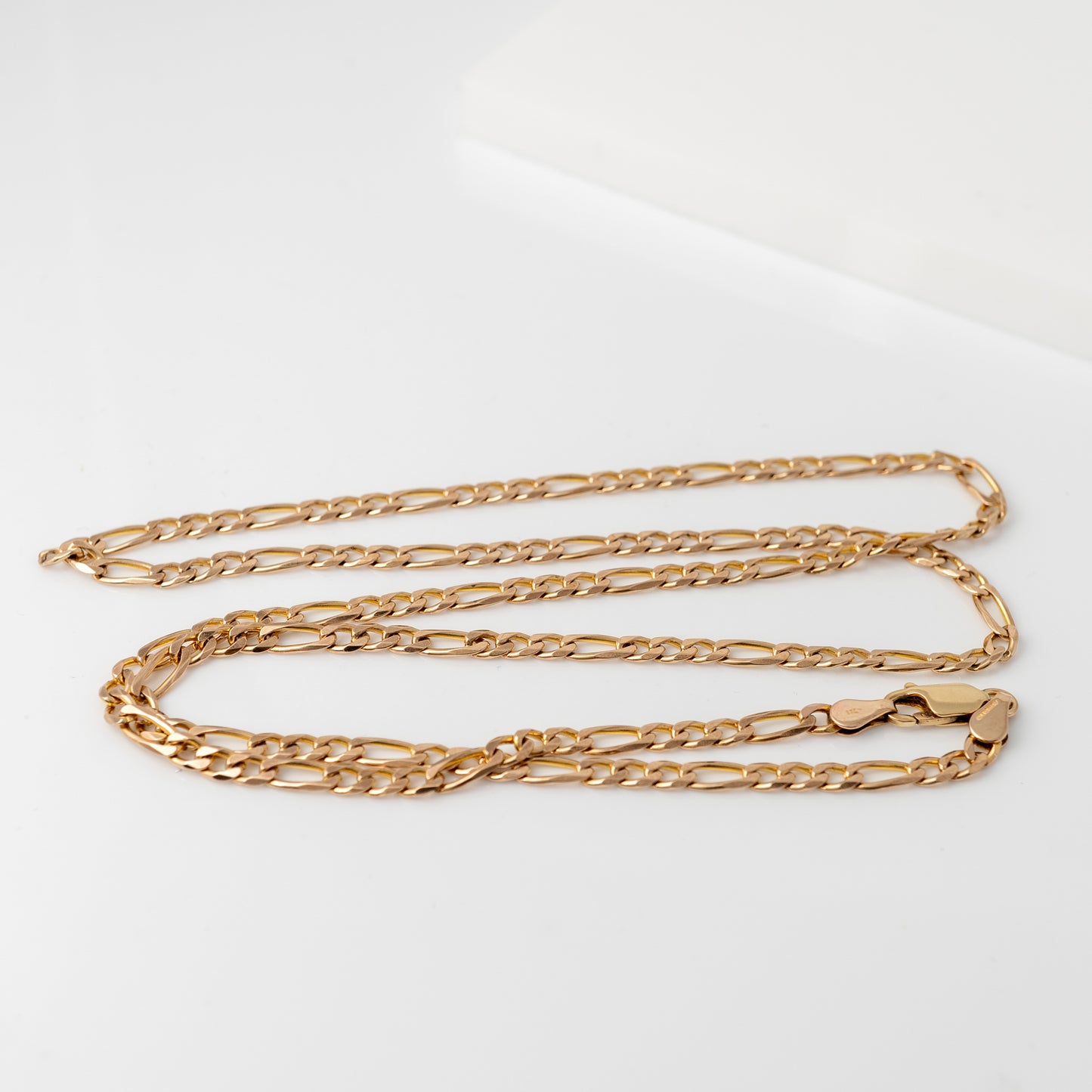 Women’s 9ct gold Figaro chain necklace on white surface. 