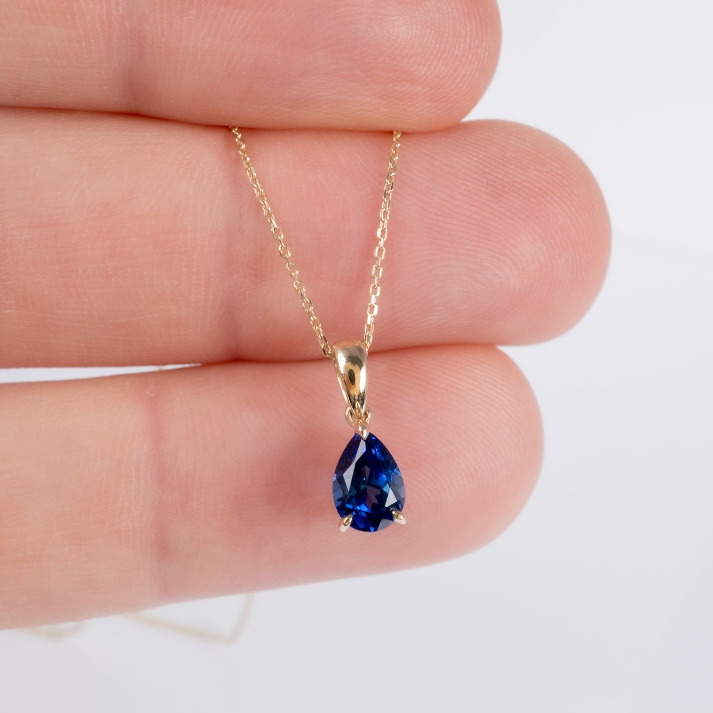 gold sapphire necklace held by fingers