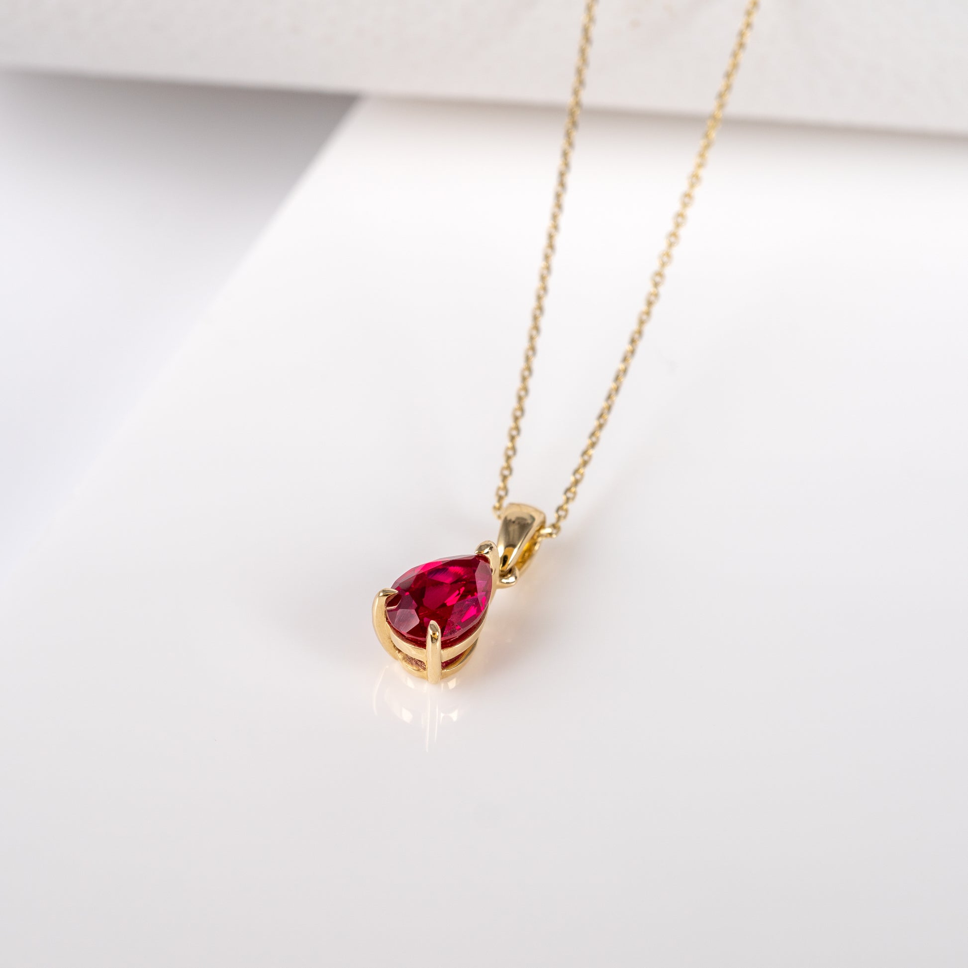 Ruby teardrop pendant necklace displayed flat, featuring lab-grown ruby in 9ct yellow gold with adjustable chain.
